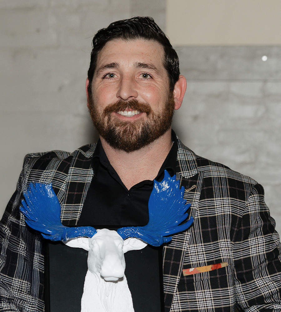 Jeremy Pflug dressed in a plaid suit holding up an award of a moose with blue antlers at the christmas party.