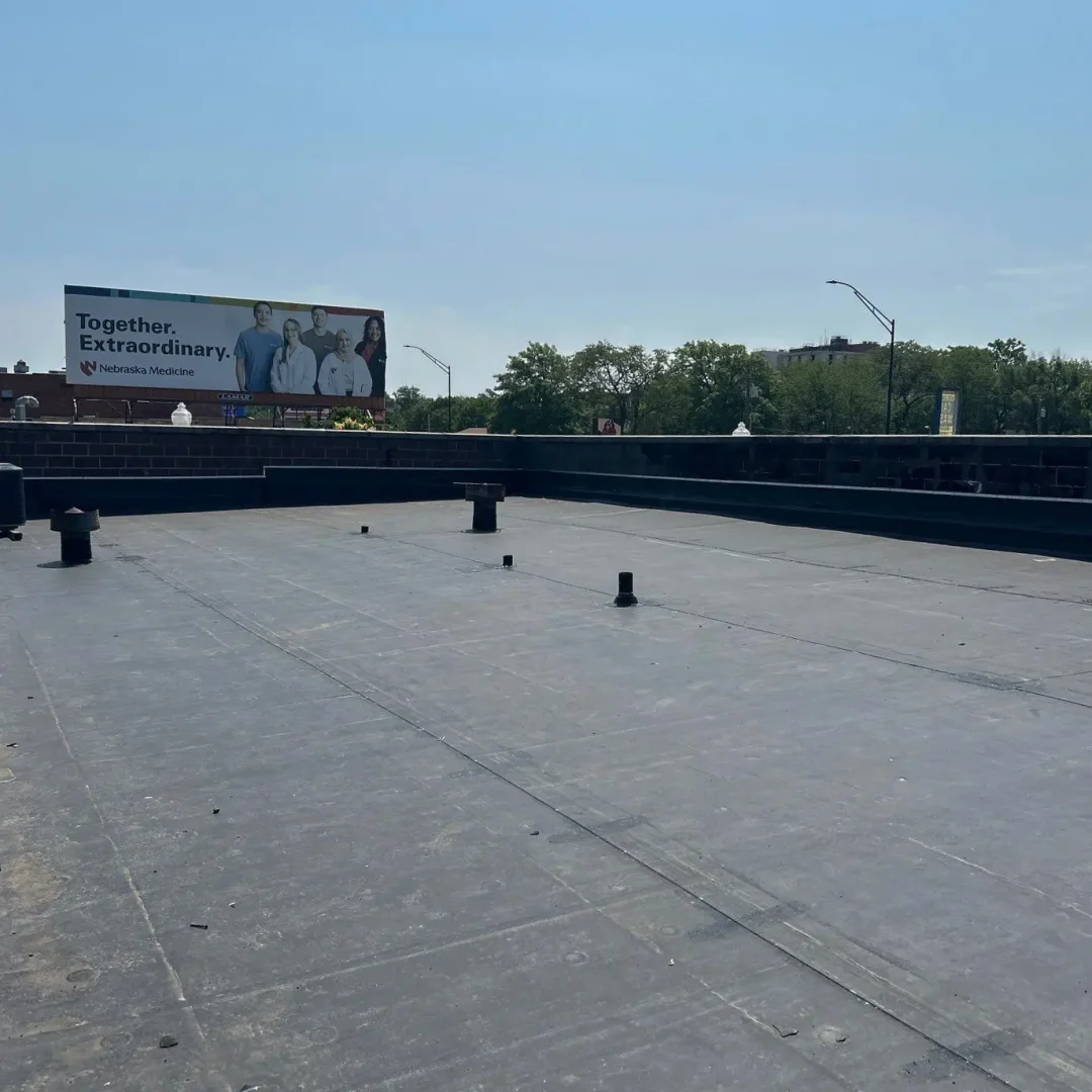 Flat commercial roof under clear skies with trees and a billboard nearby.