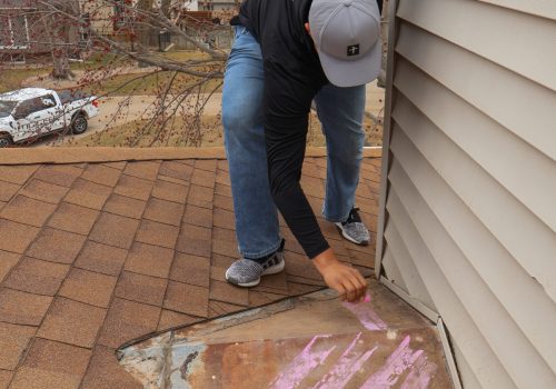 Roofer inspecting a shingle roof for damage near a house siding.