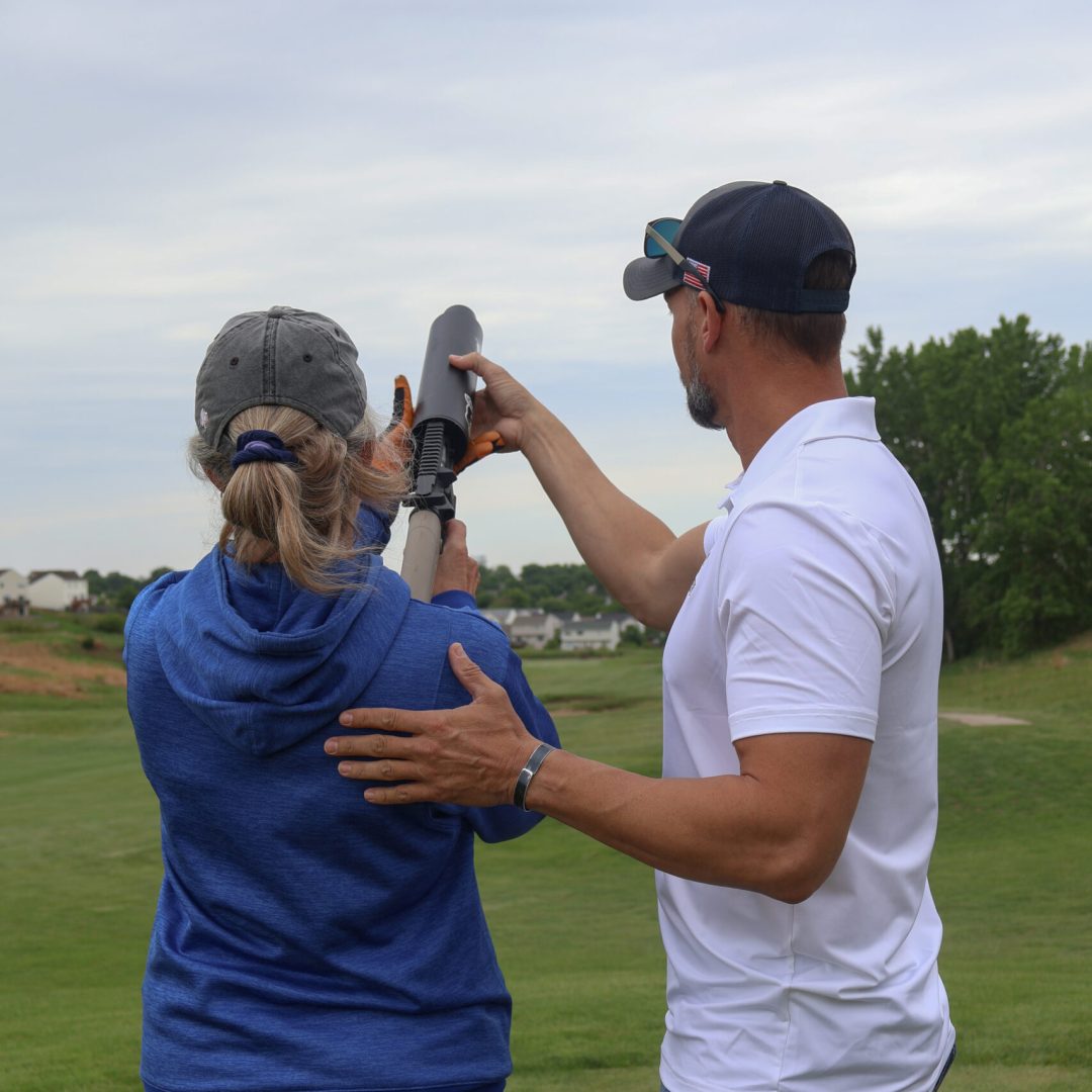 Two people on a grassy field aiming a launcher under an overcast sky.