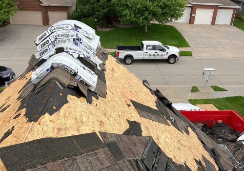 Roof under construction with shingles stacked on top; a roofing truck is parked on the street below.